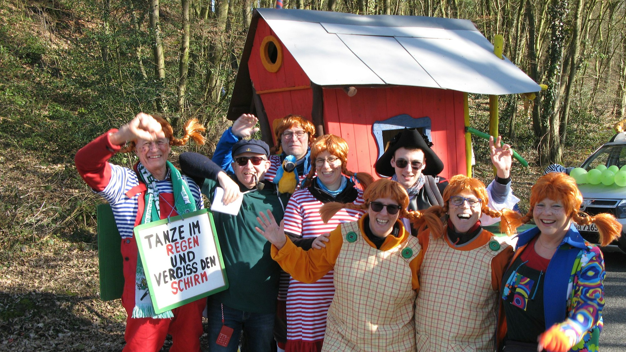 Acht Personen in Pippi Langstrumpf-Kostümen vor einem Häuschen winkenn und lachen.