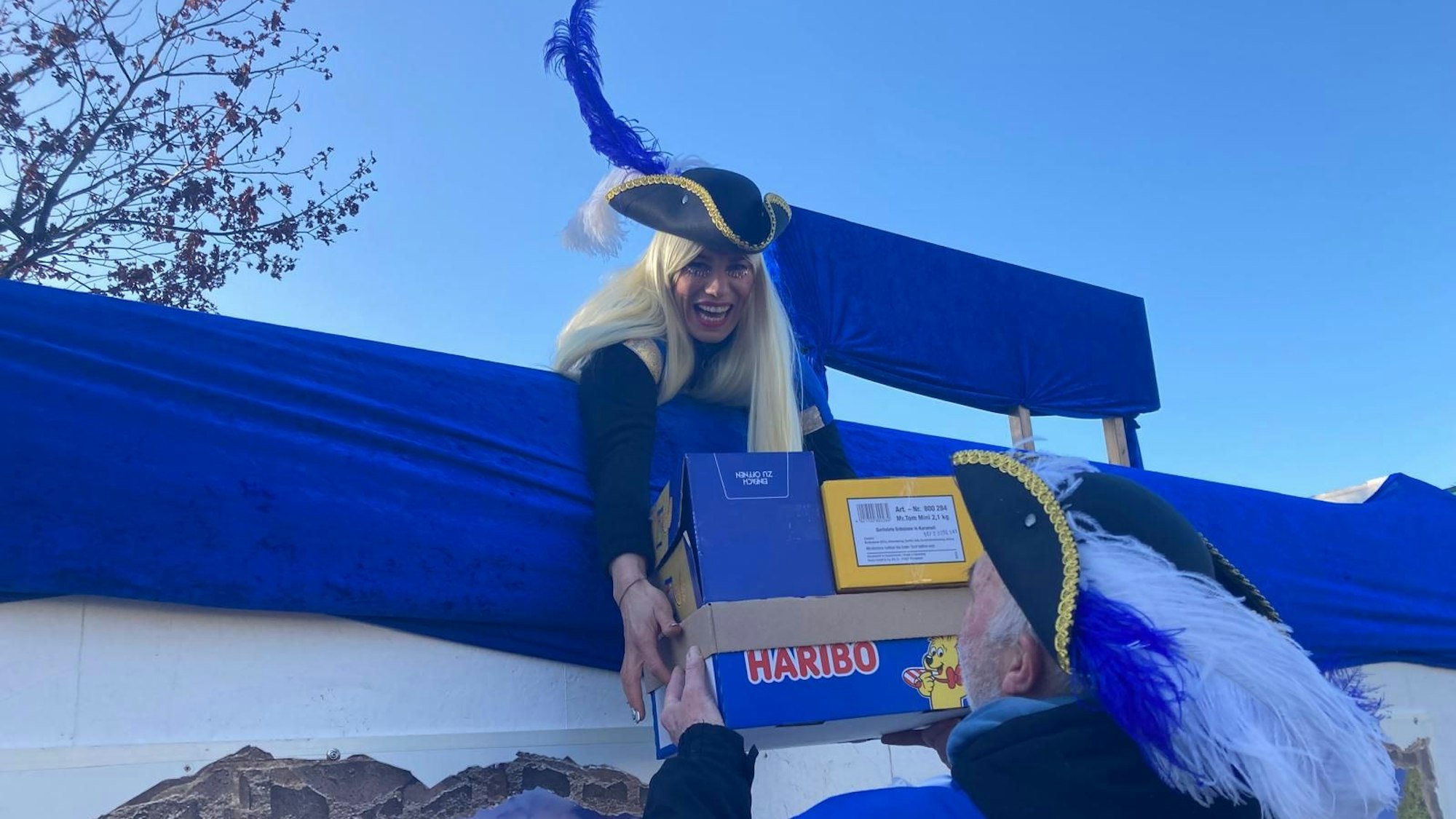 Ein Karnevalist übergibt einer Jecken einen Karton voller Süßigkeiten.