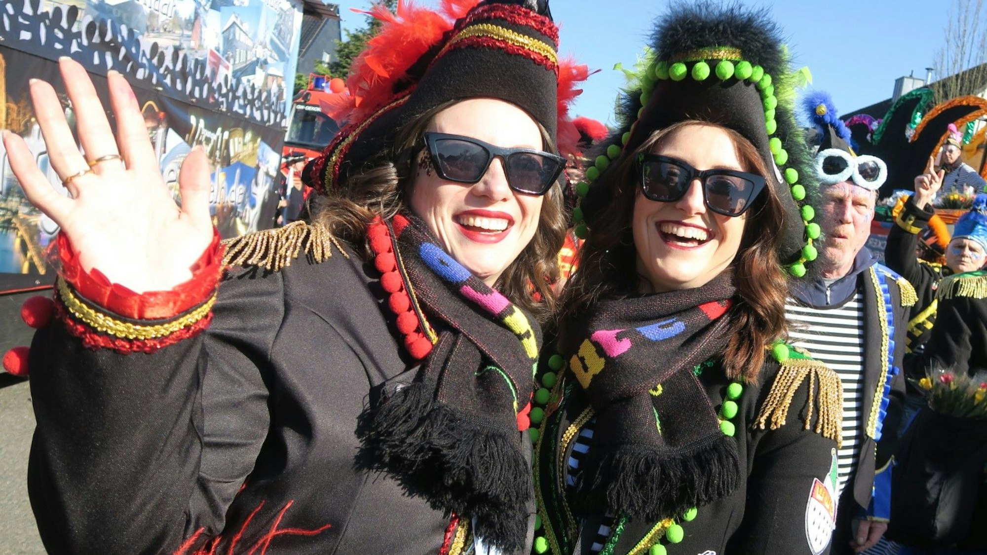 Zwei junge Frauen in Musketier-Kostümen winken lachend in die Kamera.