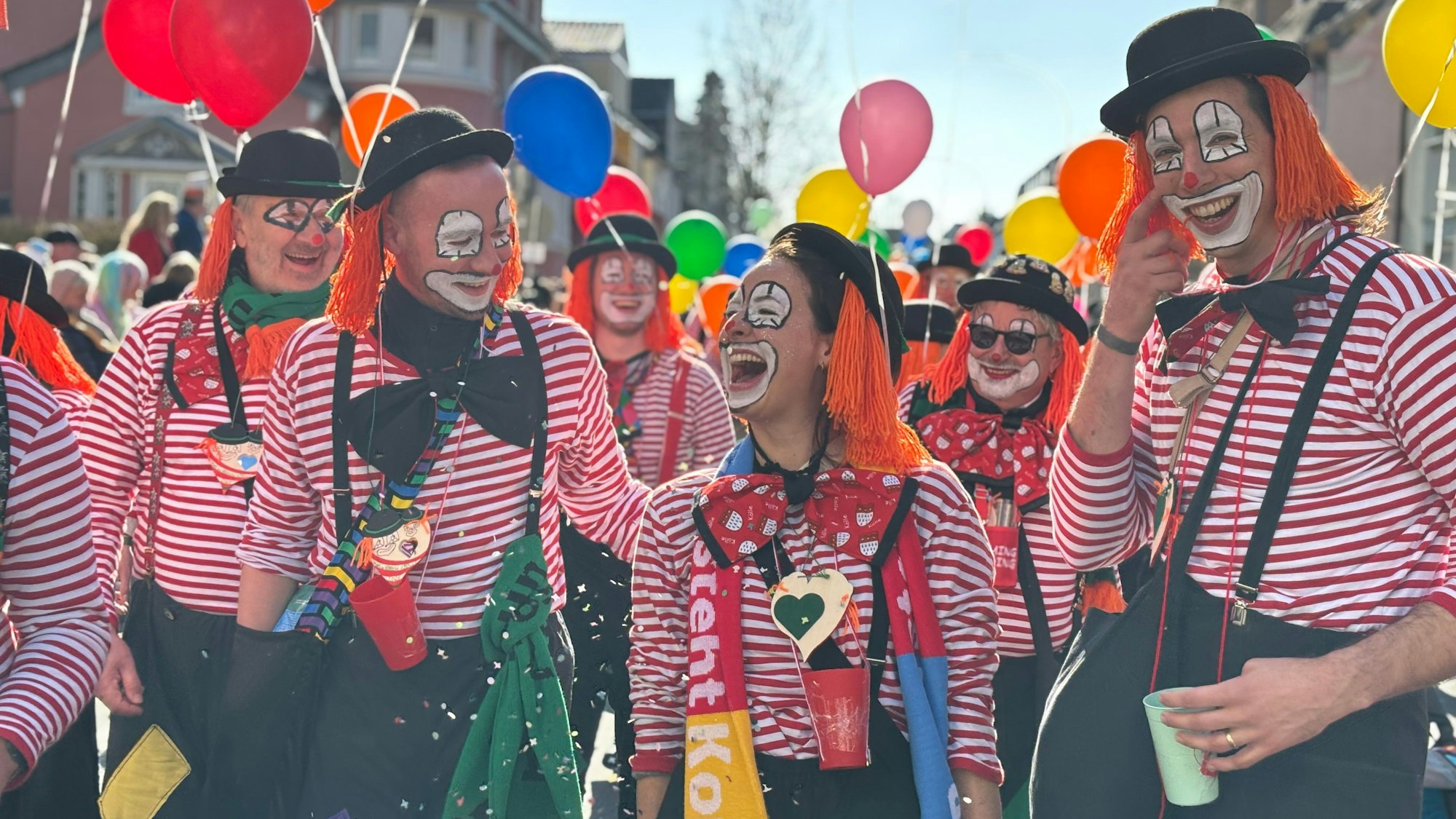 Menschen, die sich als Clowns kostümiert haben, lachen breit, während Konfetti fliegt.