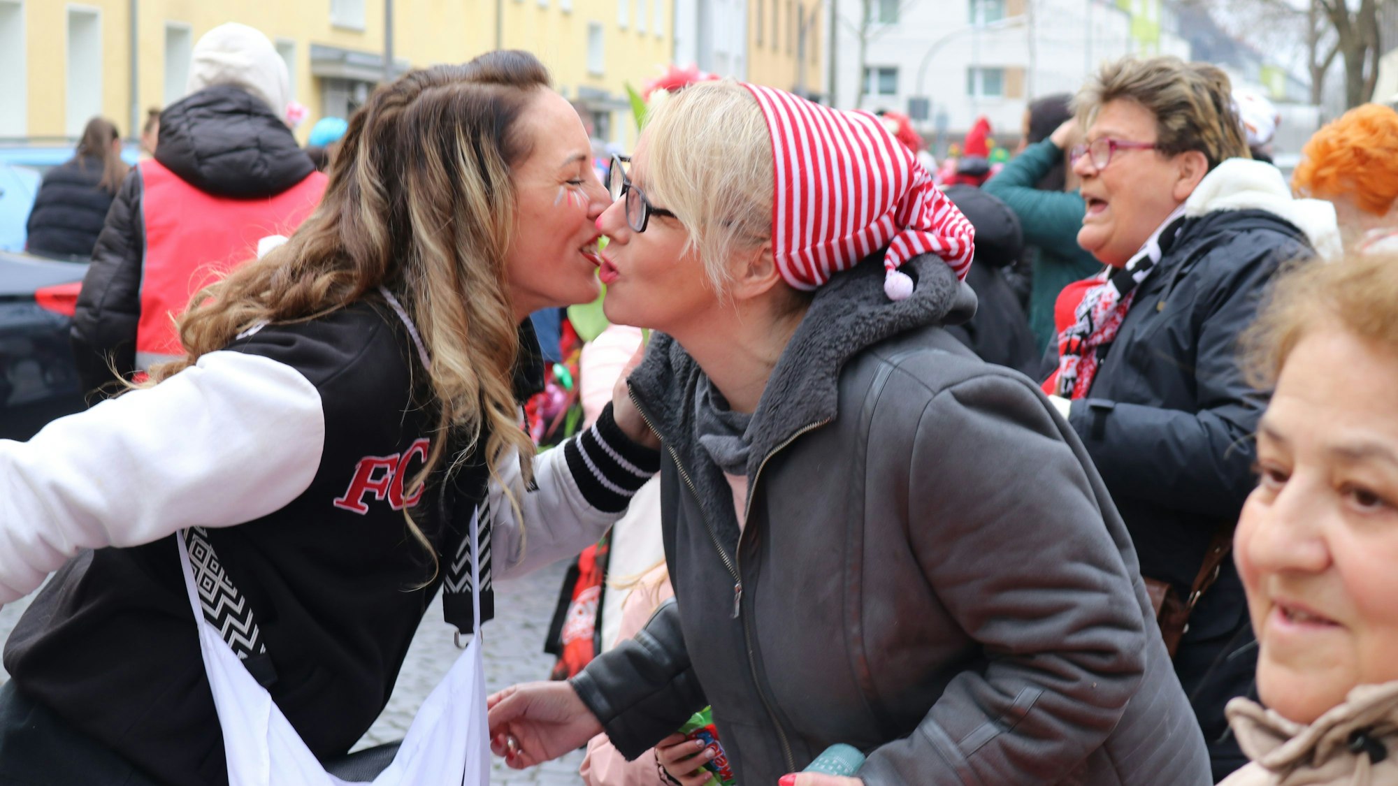 Viele Jecke stehen am Zugweg, eine Teilnehmerin küsst eine Zuschauerin auf die Wange.