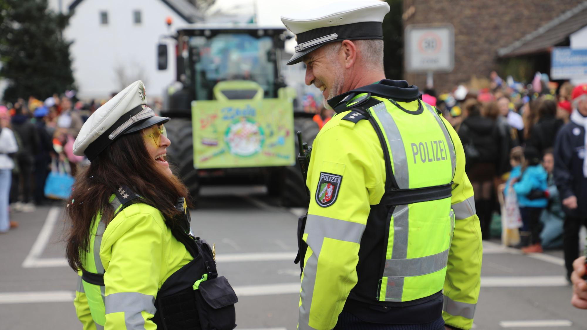 Zwei Polizisten stehen vor dem „Dr Zoch kütt“-Wagen des Refrather Karnevalszugs und lachen entspannt.