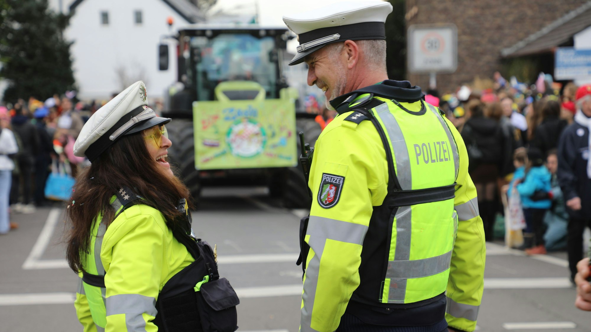 Zwei Polizisten stehen vor dem „Dr Zoch kütt“-Wagen des Refrather Karnevalszugs und lachen entspannt.