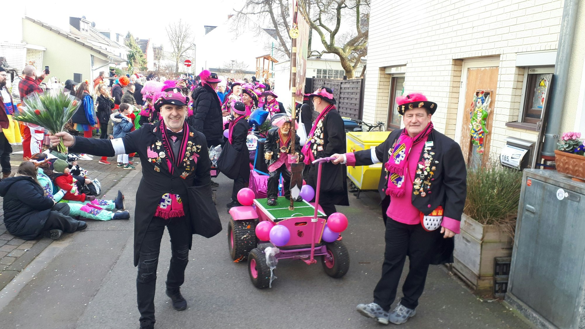 Eine Gruppe schwarz-lila gekleideter Jecken zieht durch eine schmale Straße.