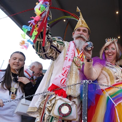 Das Foto zeigt drei Menschen hinter einer Bühnenabsperrung, die die Becher heben.