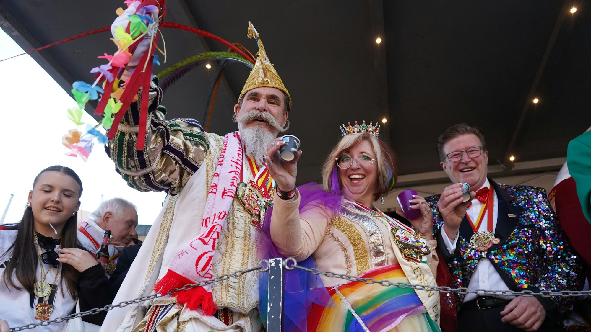 Das Foto zeigt drei Menschen hinter einer Bühnenabsperrung, die die Becher heben.