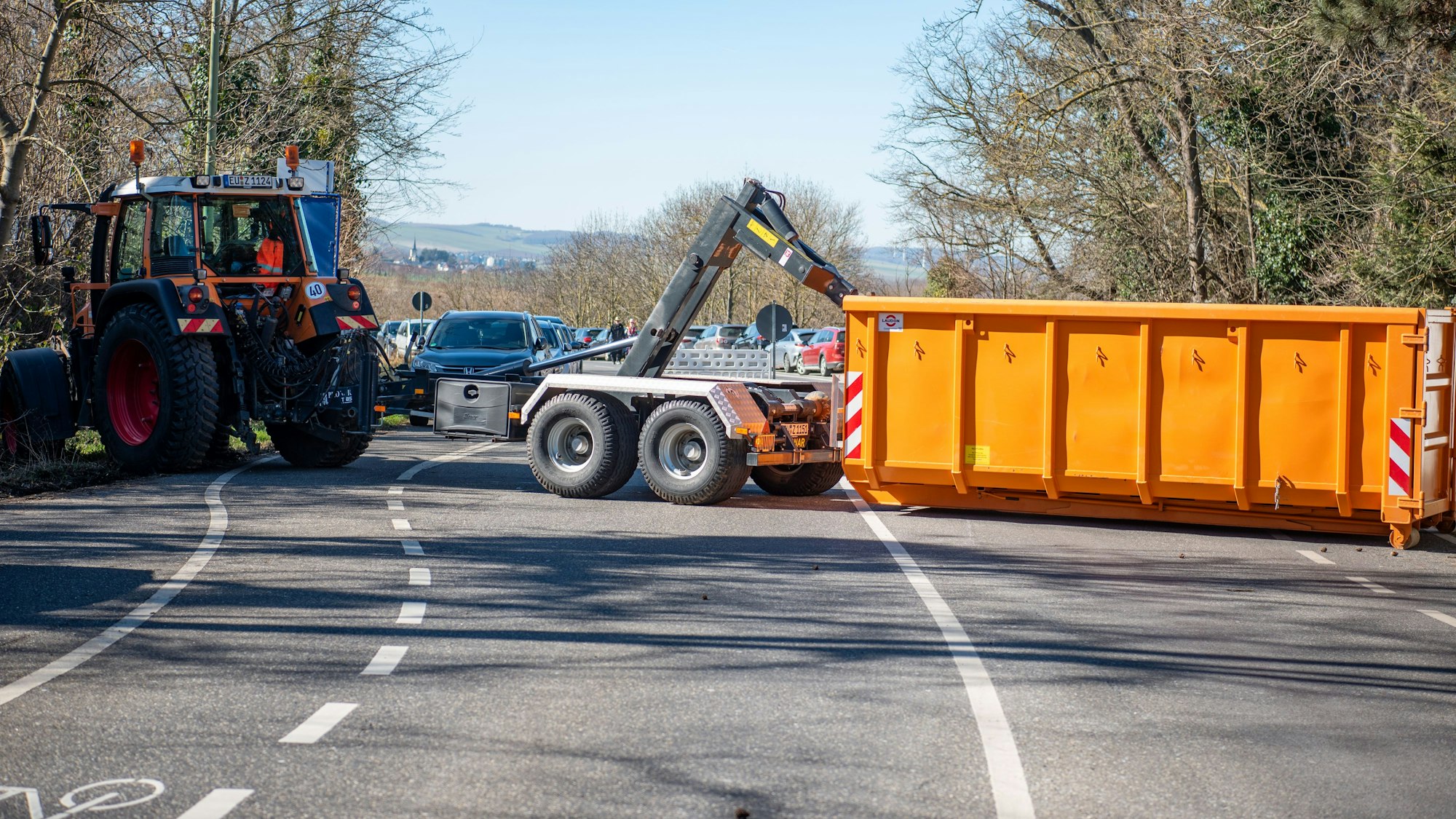 Ein Traktorfahrer lädt einen orangefarbenen Container auf einer Zufahrtsstraße in Zülpich ab.