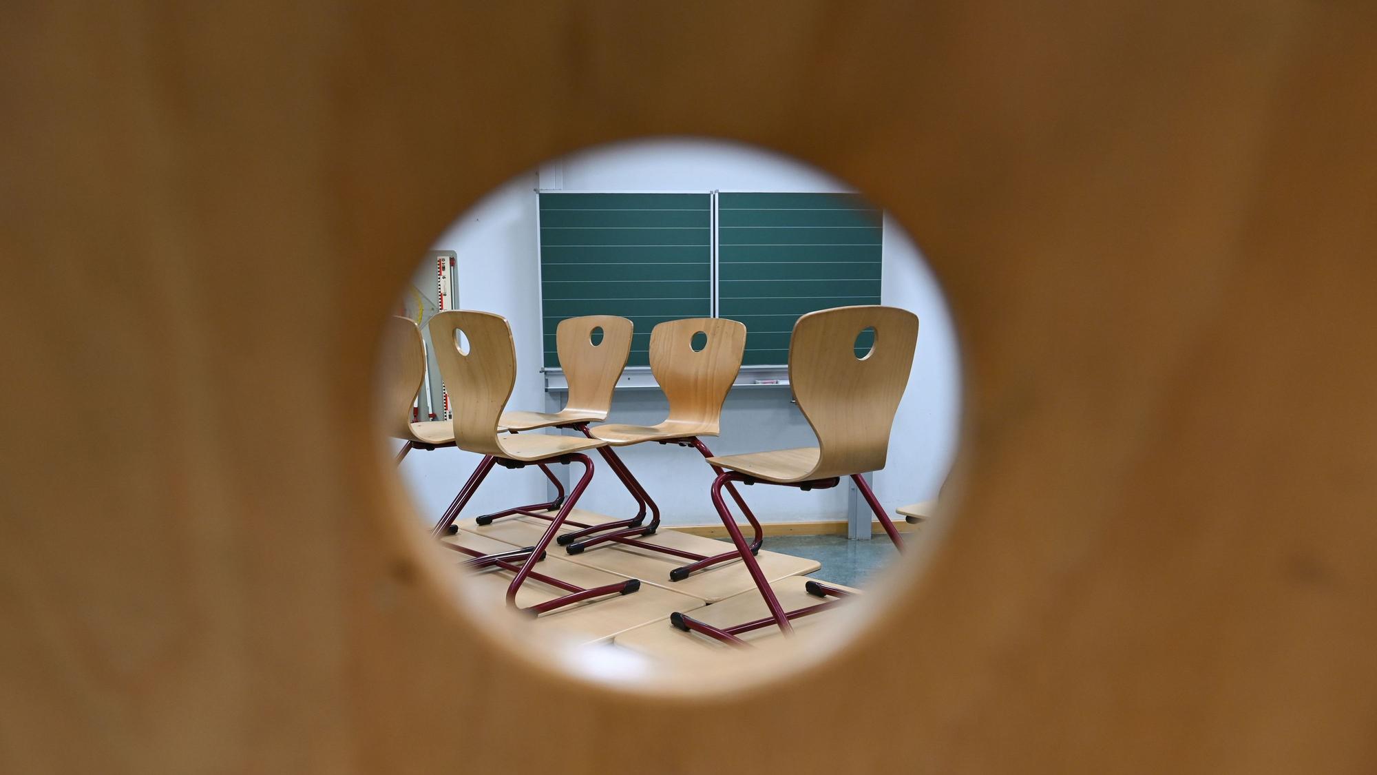 Durch das Loch in einer Stuhllehne sind in einem Klassenzimmer Stühle zu sehen, die auf Tischen stehen.