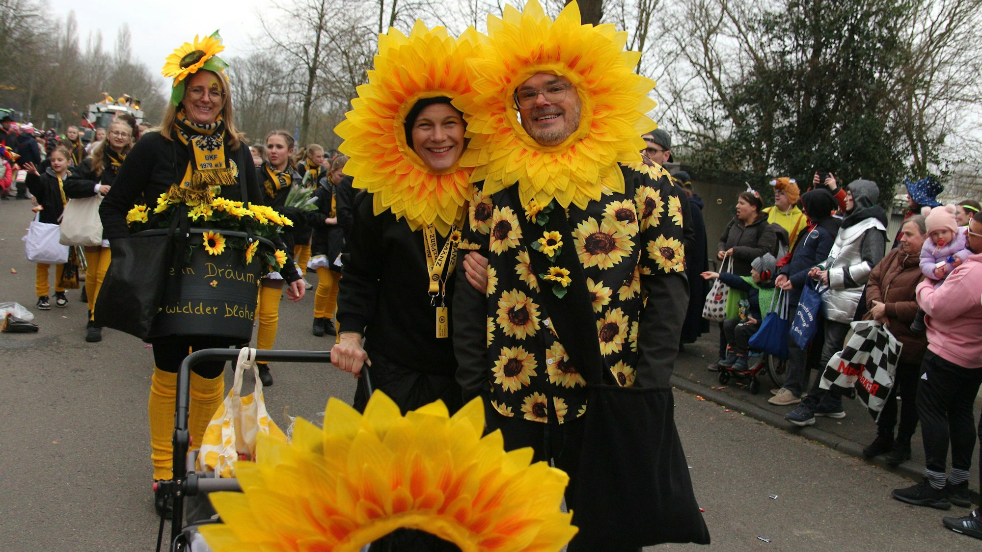 Auf dem Bild ist ein Paar zu sehen, das große Sonnenblumen-Blüten als Kopfschmuck trägt.