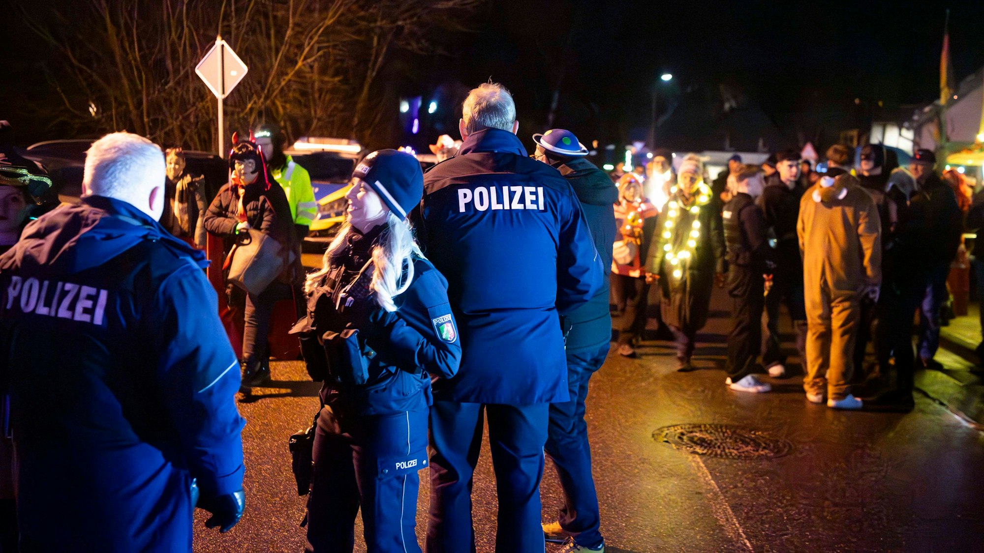 Mehrere Polizisten stehen beim Lichterzug in Eiserfey auf der Straße und beobachten, wie die Jecken friedlich feiern.