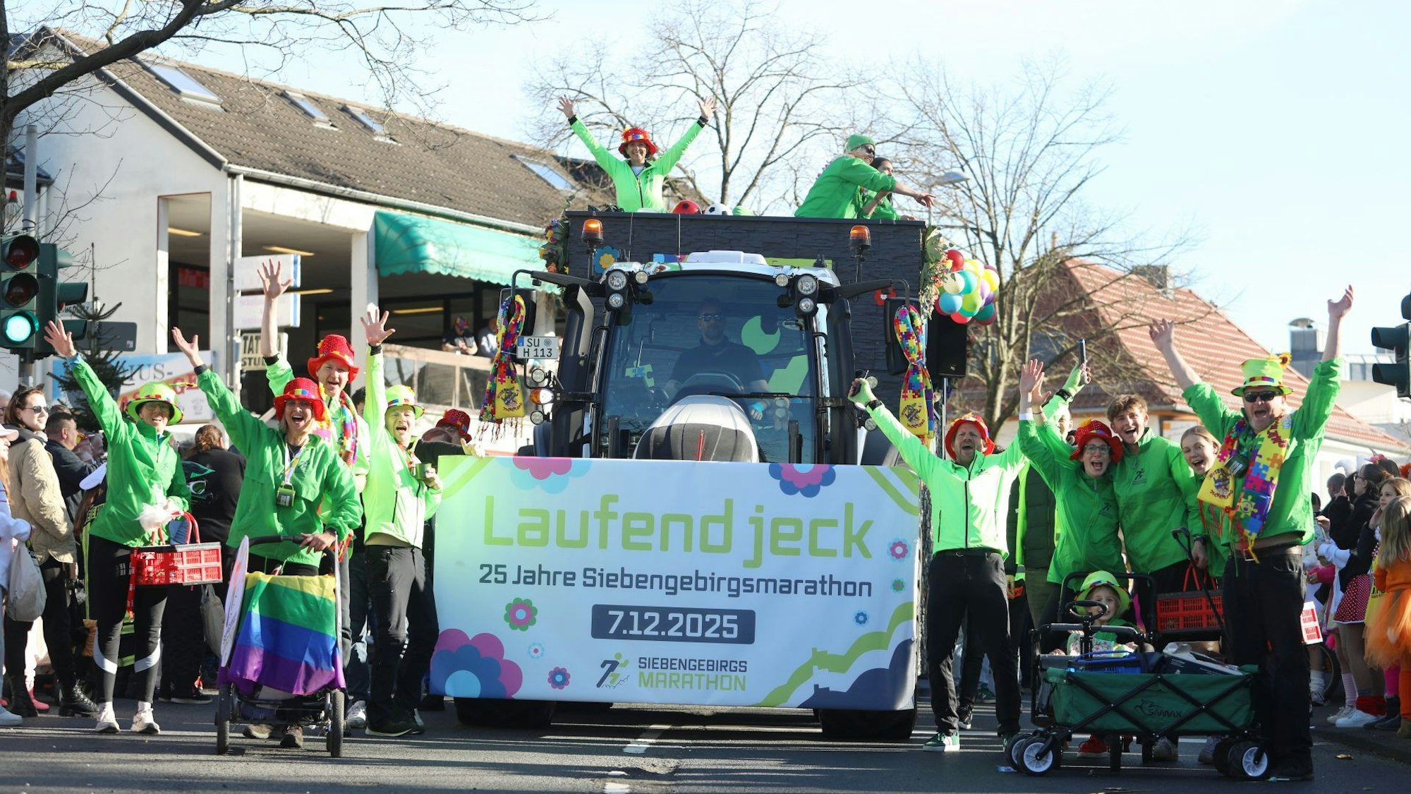 Ein Traktor mit einem Schild und dem Schriftzug "Laufend jeck", links und rechts daneben Menschen in grüner Kleidung.