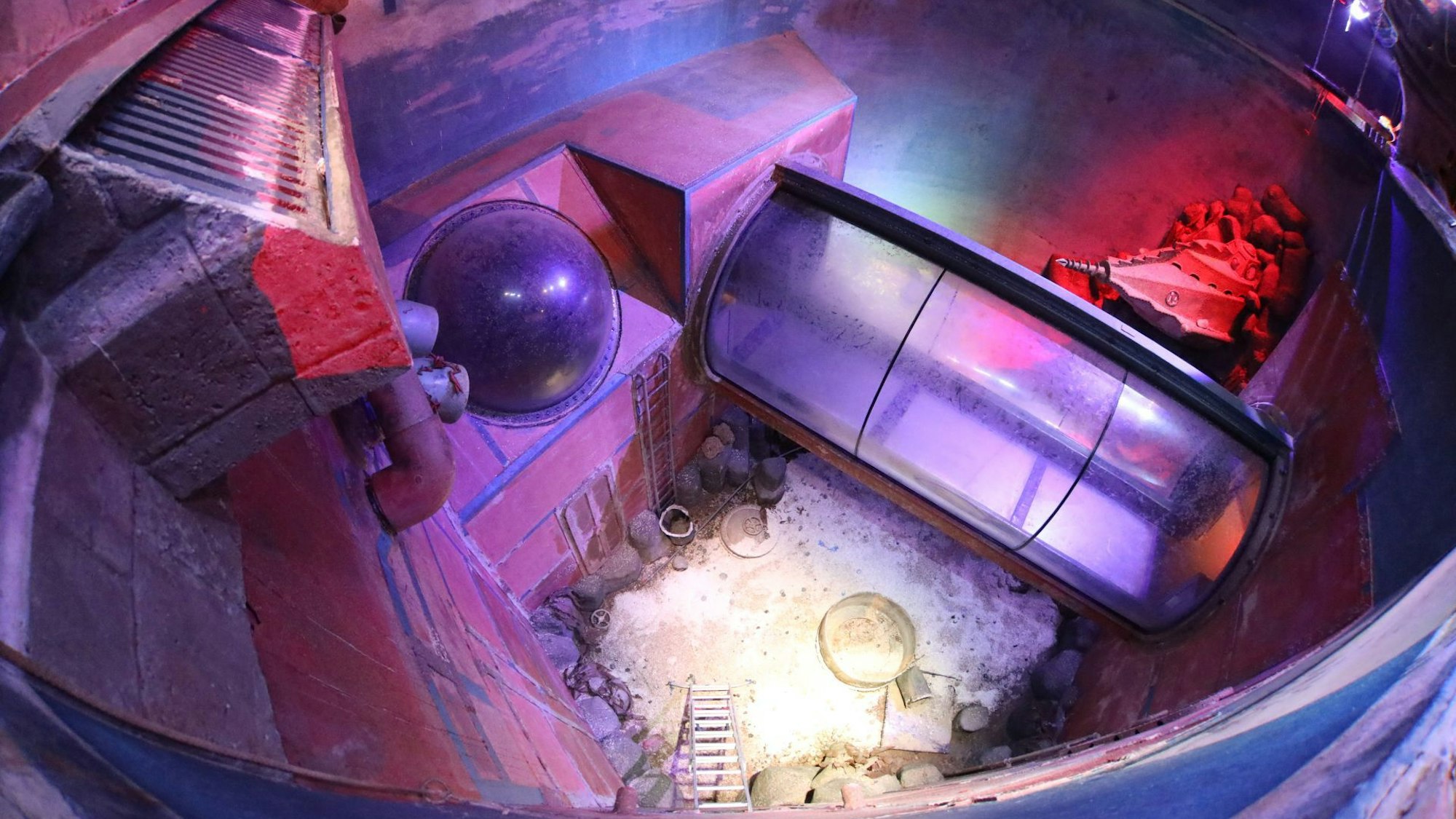 Blick in ein ehemaliges Riesenaquarium, in dem kein Wasser mehr ist. Durch das Becken verläuft eine Glasröhre.