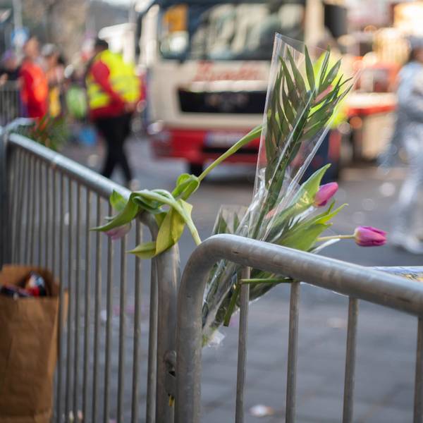 Im Rosenmontagszug in Euskirchen sind Tulpen-Sträußchen in ein Absperrgitter gesteckt. Im Hintergrund rollt ein Karnevalswagen an, verkleidete Jecke stehen auf der Straße.
