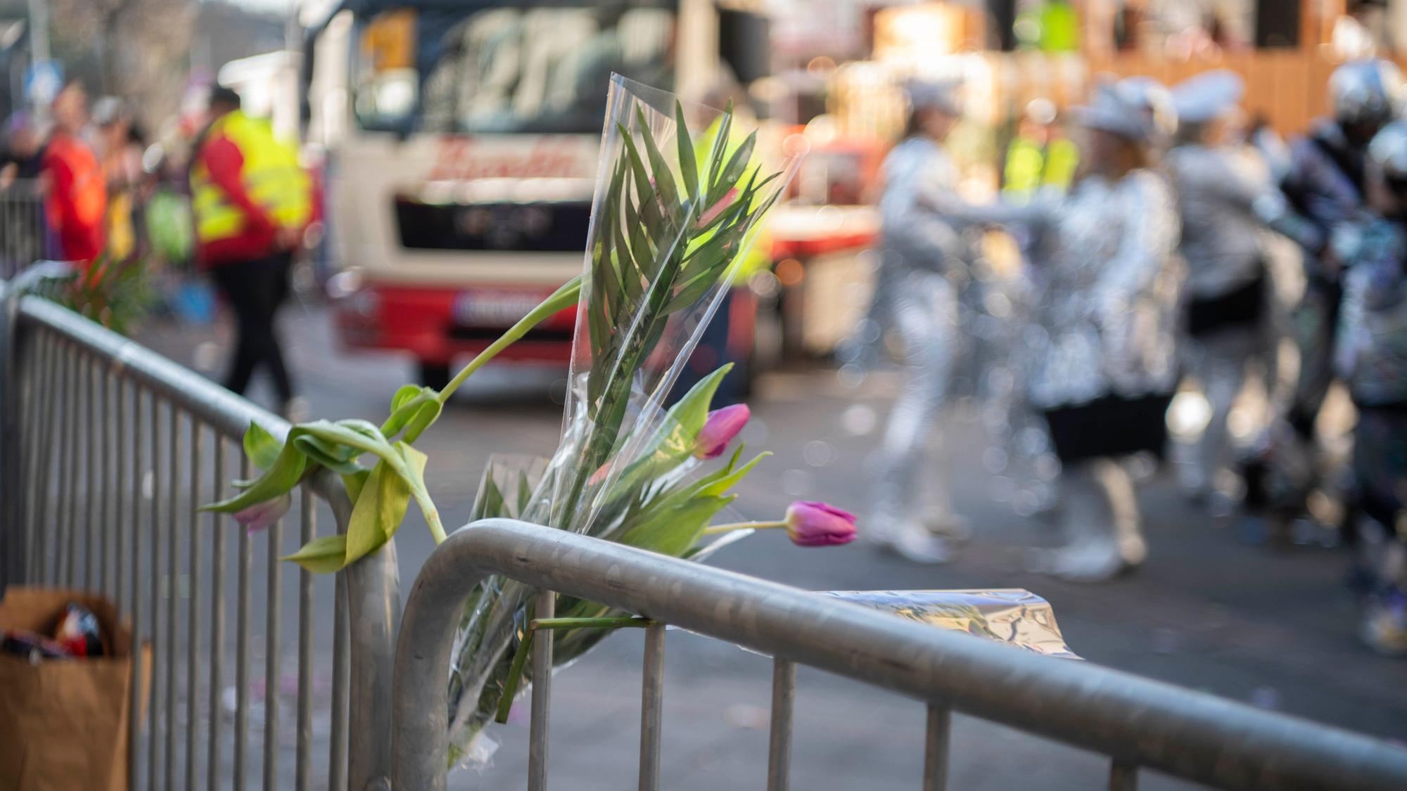 Im Rosenmontagszug in Euskirchen sind Tulpen-Sträußchen in ein Absperrgitter gesteckt. Im Hintergrund rollt ein Karnevalswagen an, verkleidete Jecke stehen auf der Straße.