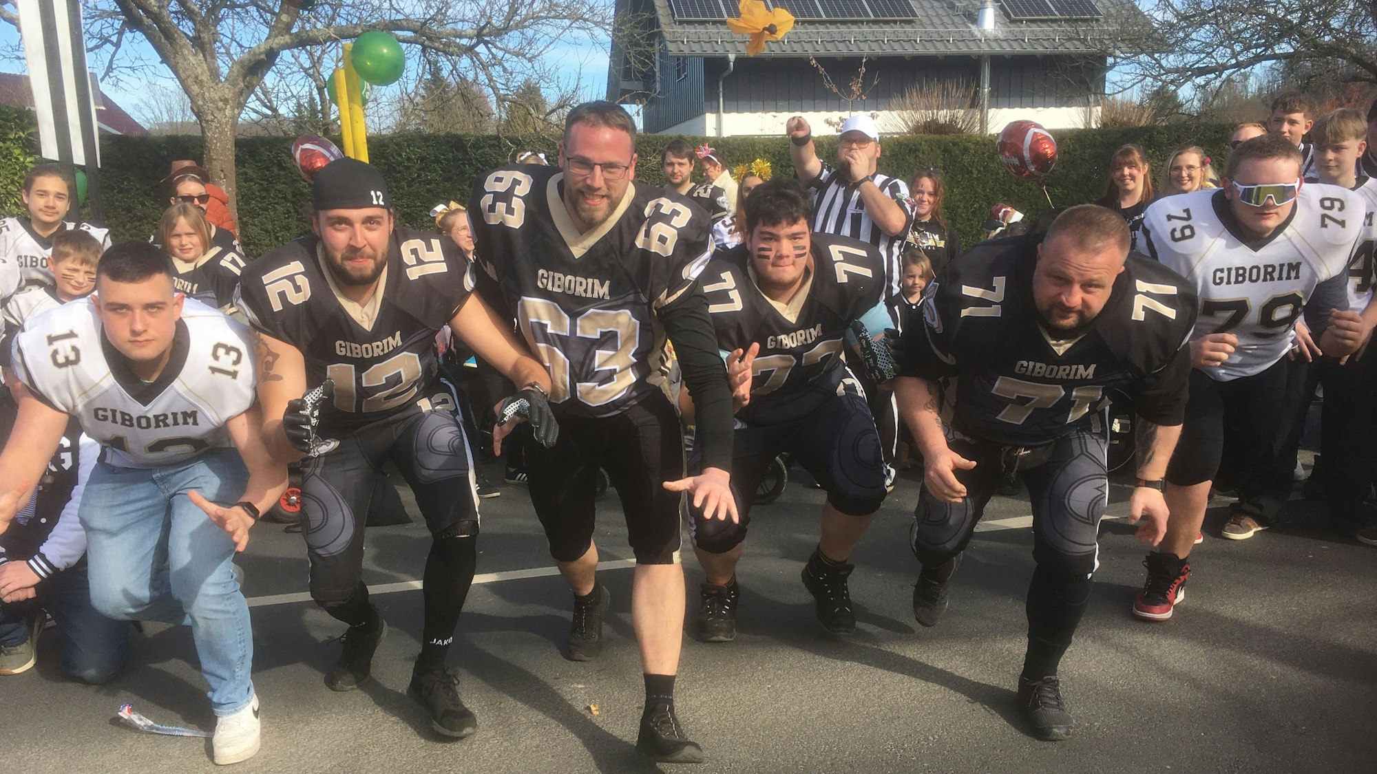 Fünf Männer in Football-Sportmontur laufen nebeneinander auf den Fotografen zu.