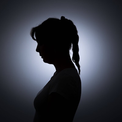 Die Silhouette einer jungen Frau zeichnet sich vor einer weissen Wand ab.