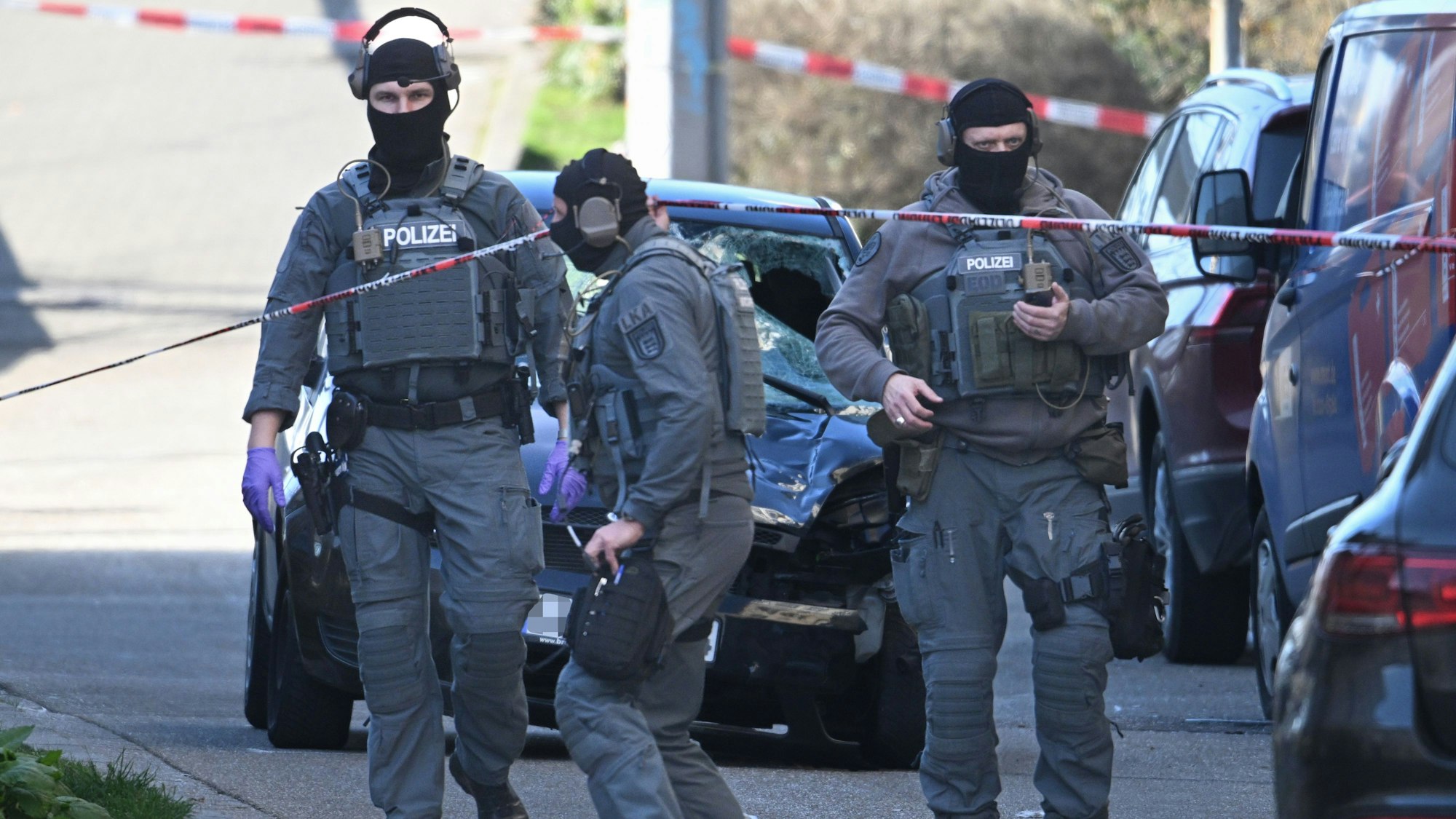 03.03.2025, Baden-Württemberg, Mannheim: Beamte des Entschärfungsdienstes der Polizei stehen in der Nähe eines beschädigten Fahrzeugs an einer Zufahrt zur Rheinbrücke. Nach einem Vorfall mit einem Auto in der Mannheimer Innenstadt mit mindestens einem Toten und mehreren Verletzten ist der mutmaßliche Fahrer nach Polizeiangaben festgenommen worden.