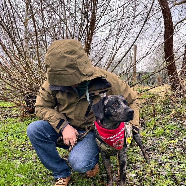 Das Foto zeigt einen Mann, der sich eine Kapuze ins Gesicht gezogen hat, mit seinem Hund.