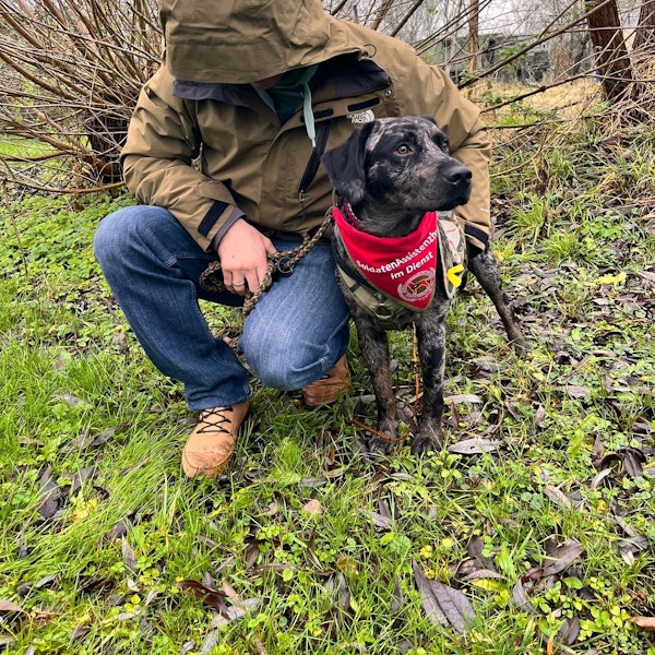 Das Foto zeigt einen Mann mit heruntergezogener Kapuze und einen Hund.