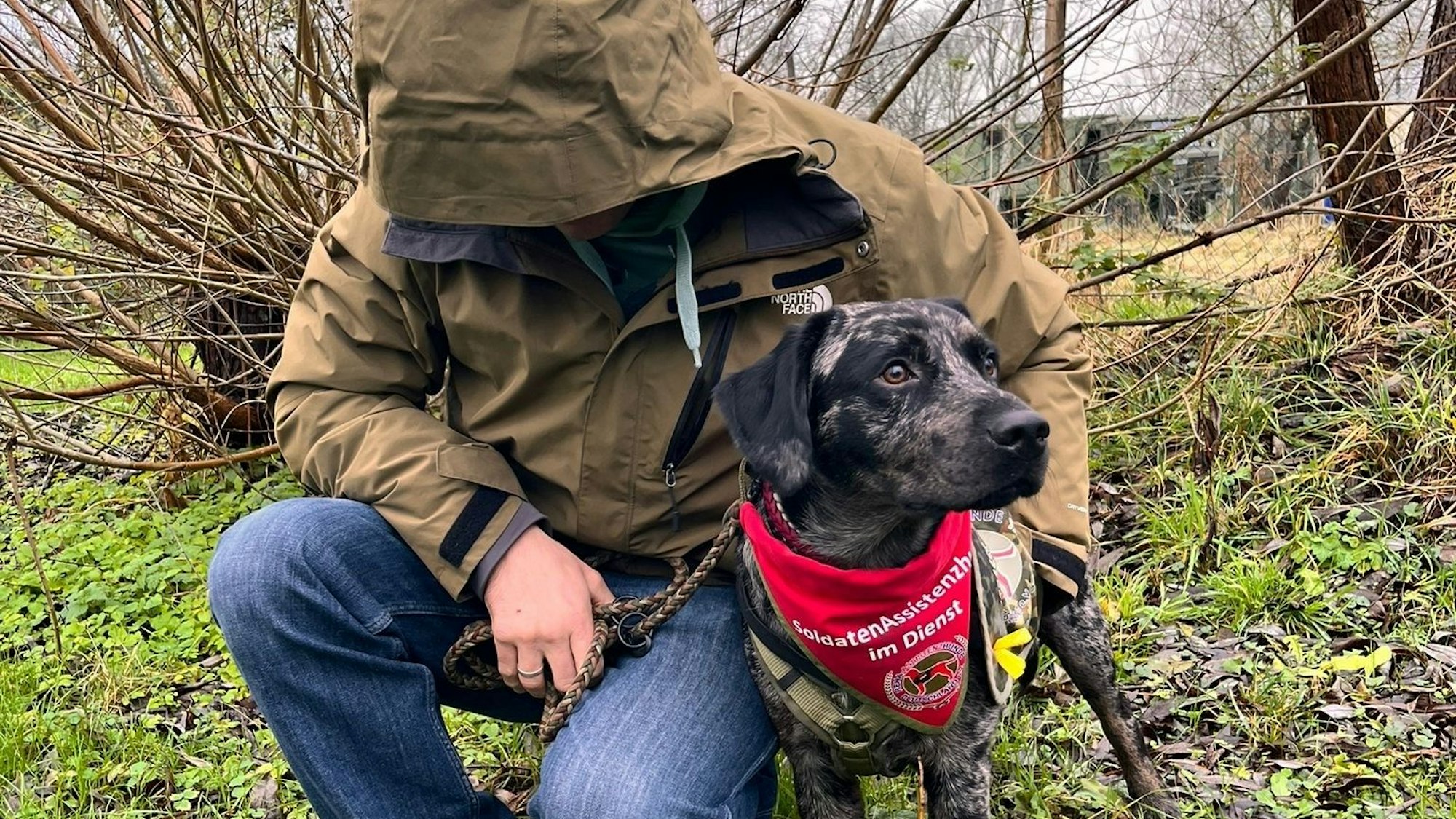 Das Foto zeigt einen Mann, der sich eine Kapuze ins Gesicht gezogen hat, mit seinem Hund.