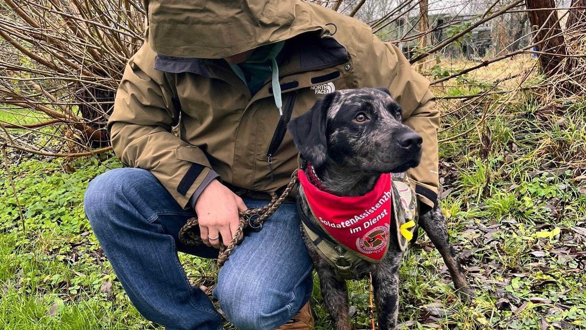 Das Foto zeigt einen Mann mit heruntergezogener Kapuze und einen Hund.