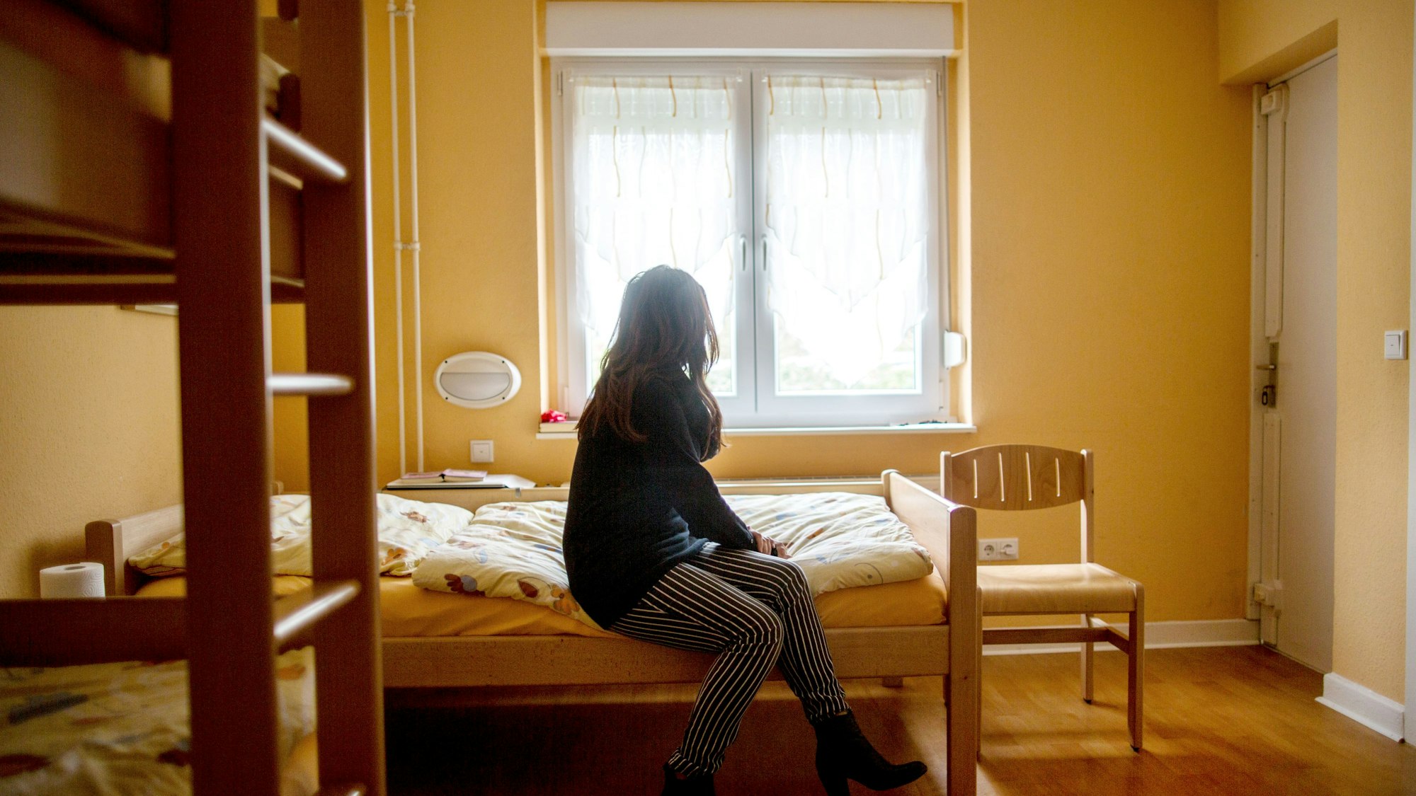 Eine Frau sitzt im Frauenhaus auf einem Bett. Das Gleichstellungsministerium in NRW möchte Frauenhäuser stärker fördern. +++ dpa-Bildfunk +++