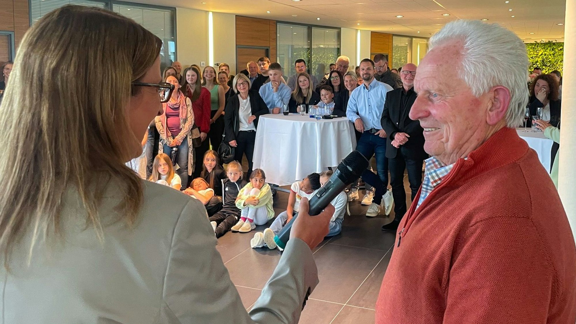 Der Sportler des Jahres 2023, Eckart Wudarzak, wird von Ramona Hammes, stellvertretende Redaktionsleiterin, interviewt. Hammes hält Wudarzak ein Mikrofon vor den Mund. Im Hintergrund sind weitere Nominierte und Zuschauer zu sehen.