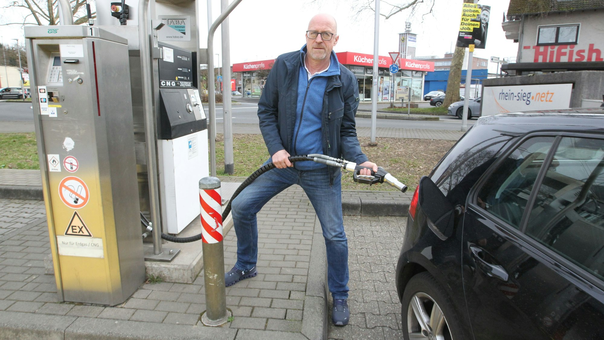 Ein Mann steht mit der Zapfpistole für Erdgas an seinem Auto.