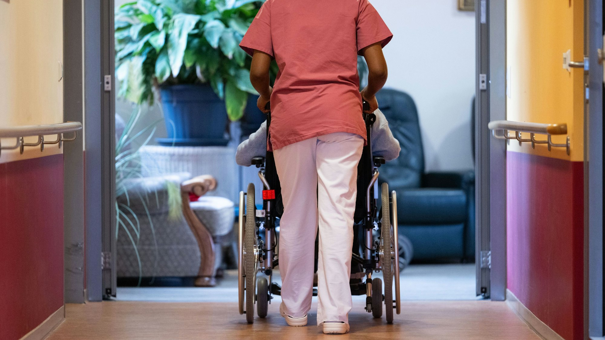 Eine Bewohnerin eines Pflegeheims wird von einer Pflegerin einen Gang entlang geschoben.