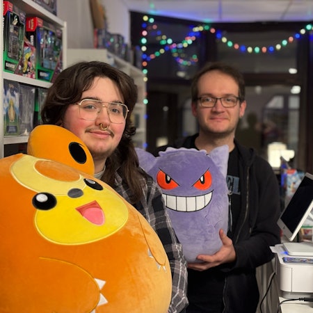 Zwei Männer mit Brillen halten Pokémon-Plüschfiguren in die Kamera.