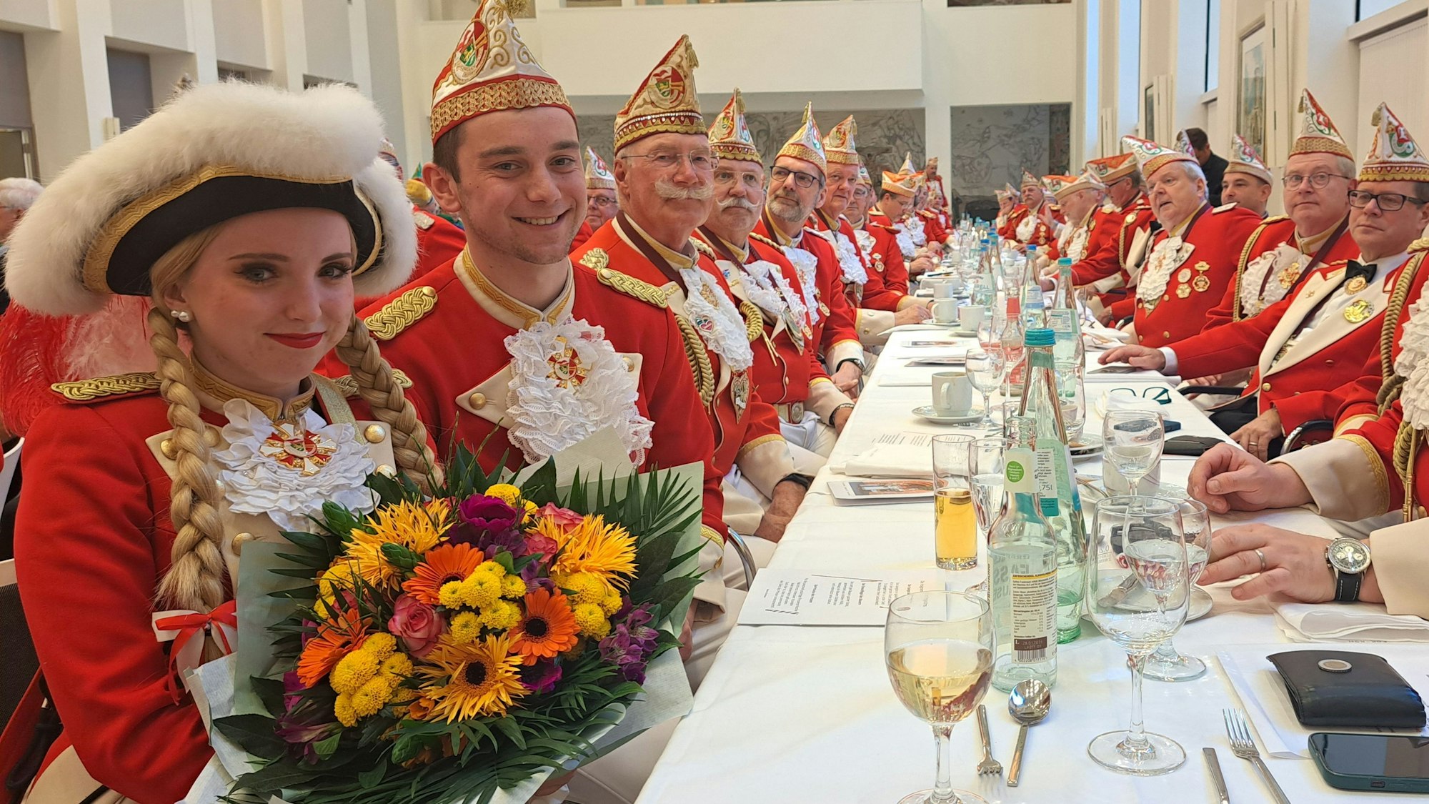 Das Tanzpaar der Prinzengarde sitzt mit den Gardisten der Prinzengarde Bergisch Gladbach an einem langen Tisch beim Prinzenessen im Kardinal-Schulte-Haus in Bensberg.