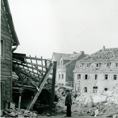 Zerbombte Häuser, Trümmer, ein Mann mit Stock, ein Haus ohne Dachpfannen.