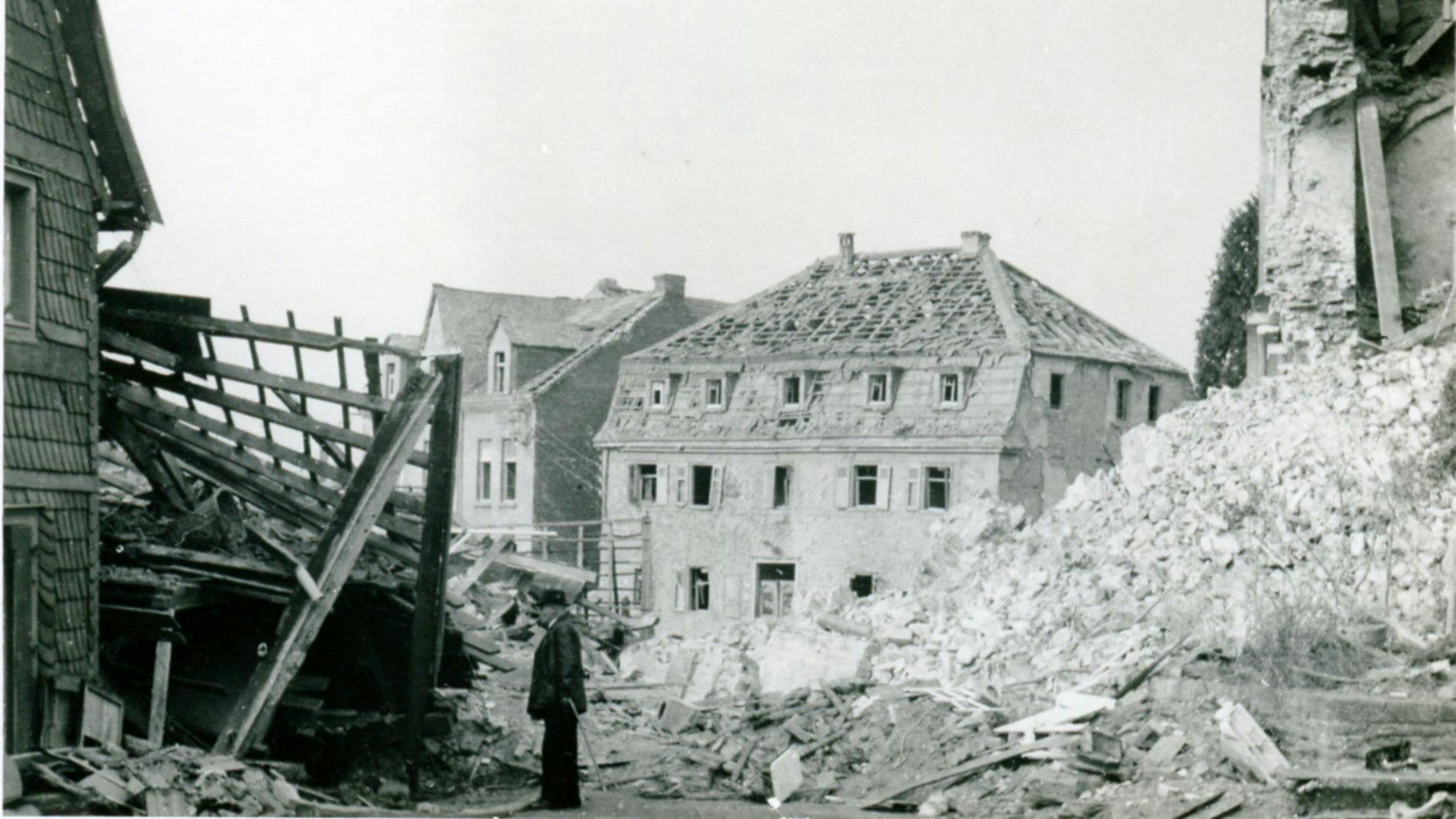 Zerbombte Häuser, Trümmer, ein Mann mit Stock, ein Haus ohne Dachpfannen.