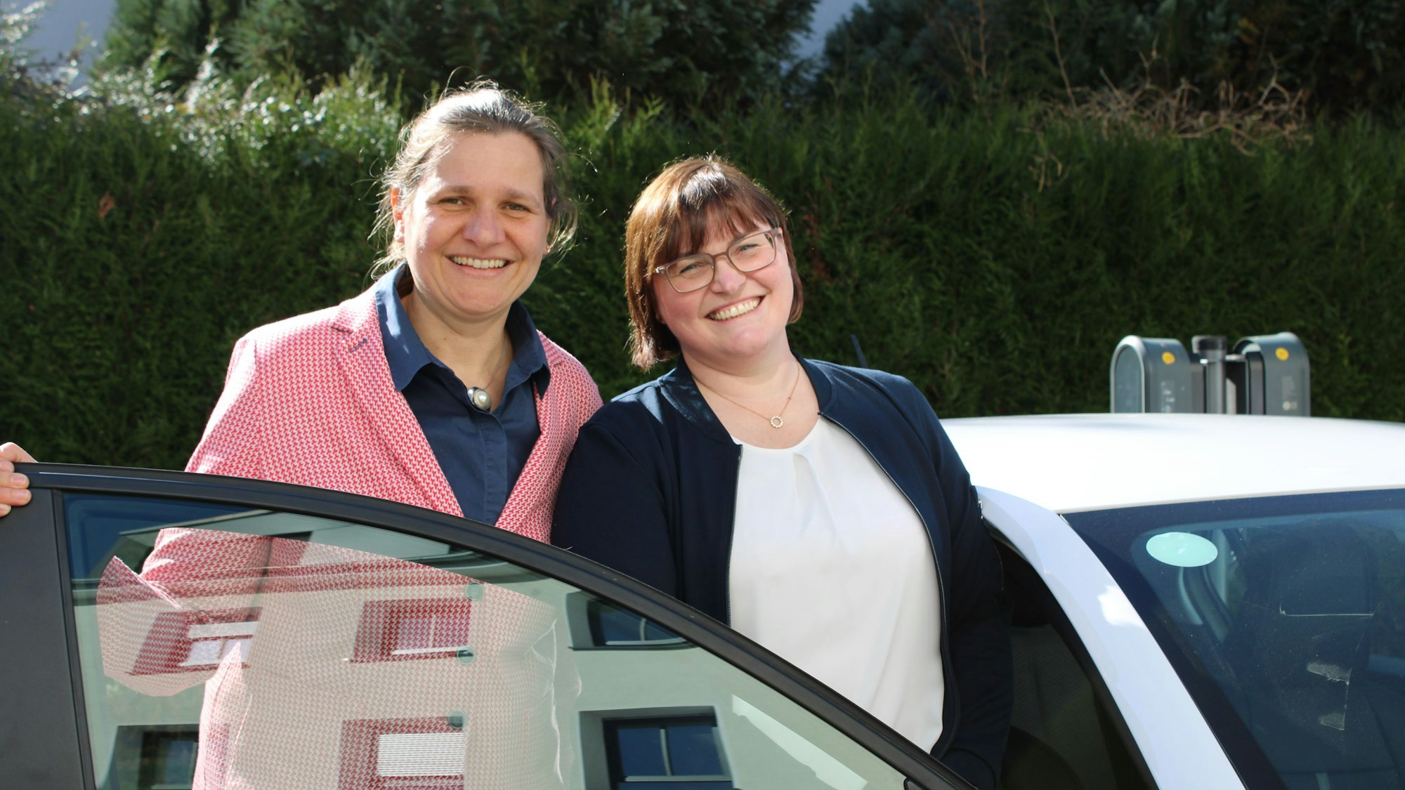 Zwei Frauen stehen lächelnd neben einem Auto.