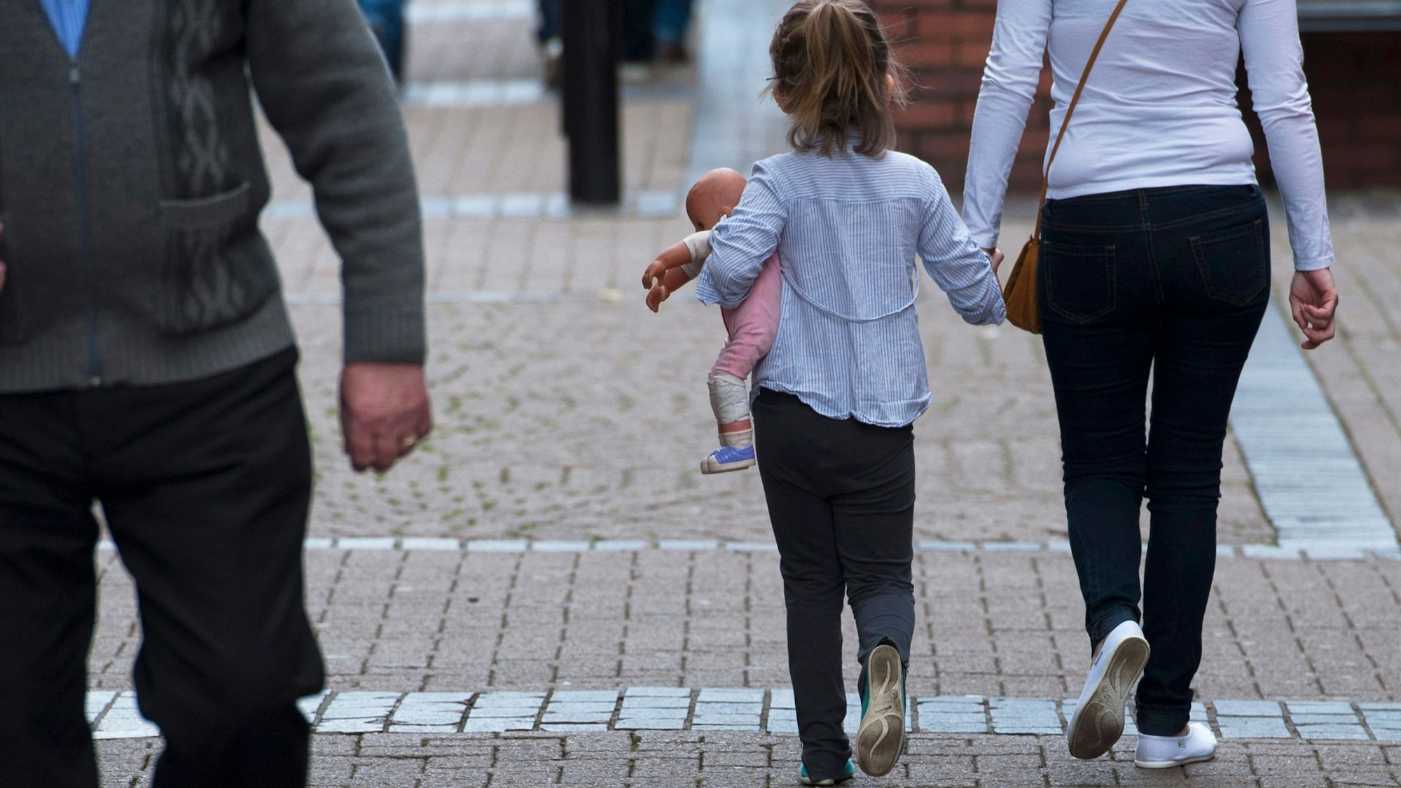 Ein junges Mädchen hält eine Puppe, während sie am 27. August 2014 Hand in Hand mit einer Frau in Rotherham, Yorkshire, Großbritannien, spazieren geht