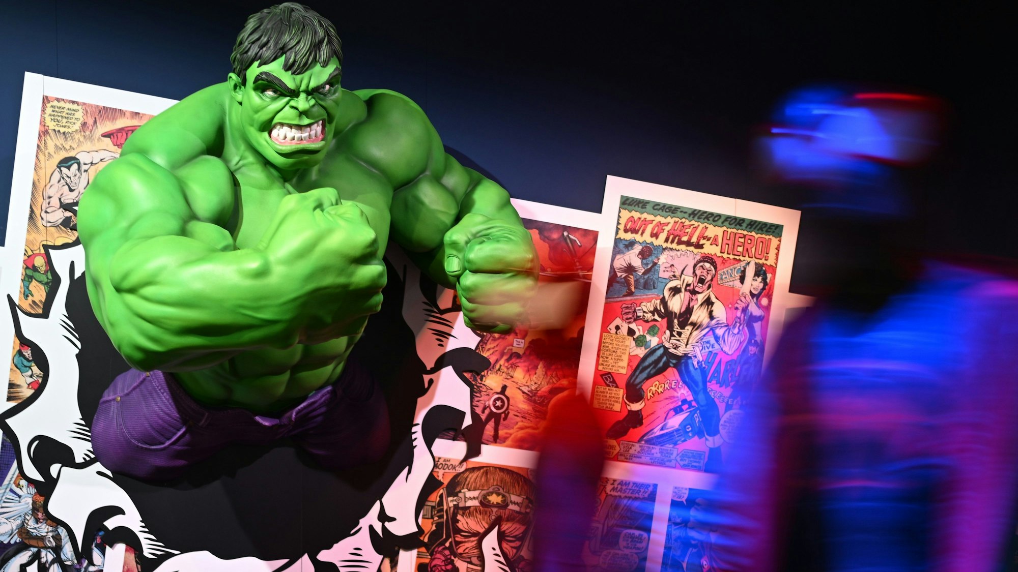 Darsteller in Spider-Man-Kostümen gehen an der Figur des Hulk vorbei. Die Marvel-Ausstellung führt vom 07.03. bis zum 22.06.2025 durch 85 Jahre Marvel-Geschichte und präsentiert mehr als 200 Exponate.