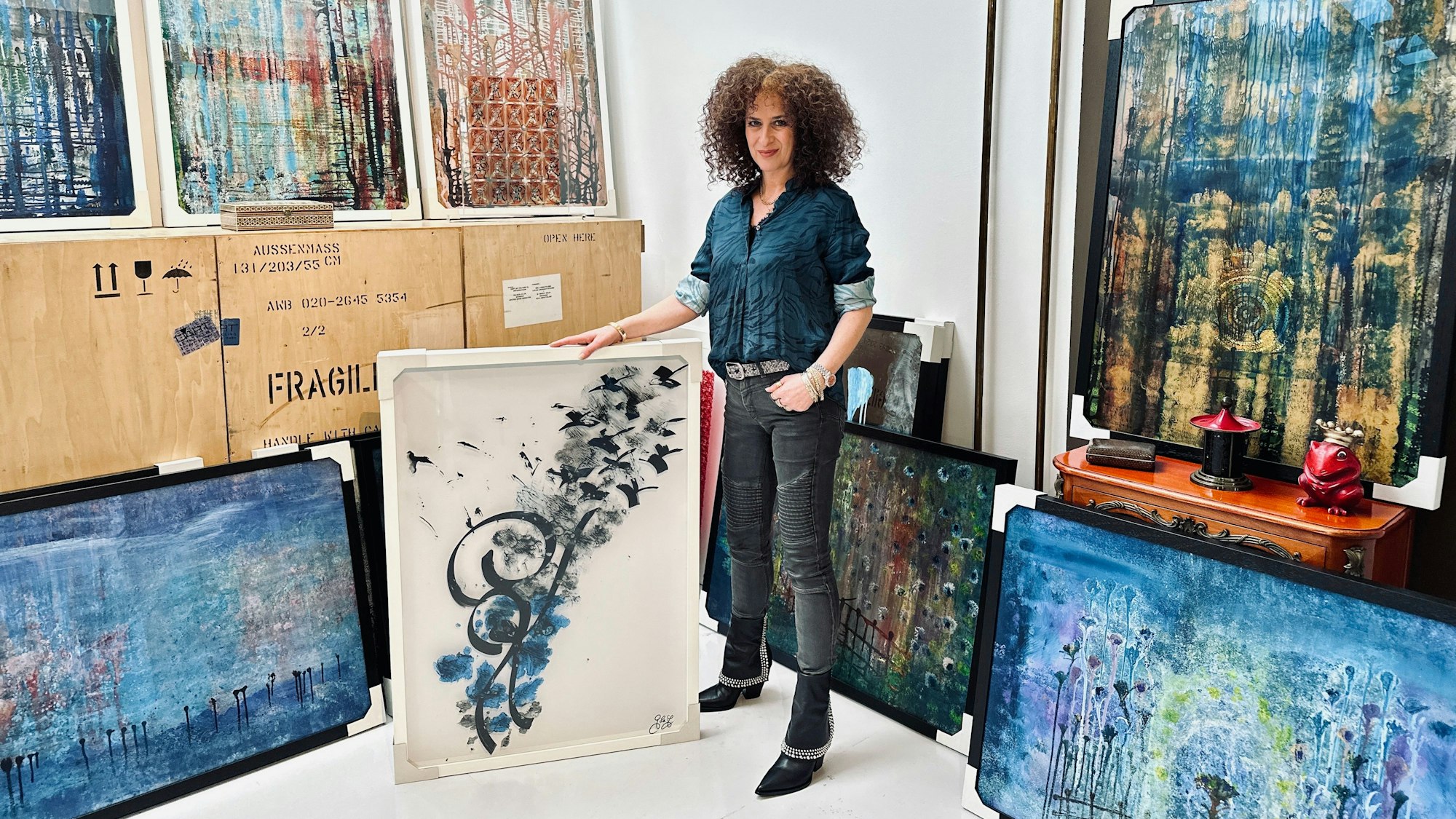 Eine Frau mit lockigem Haar steht inmitten von abstrakten großformatigen Bildern.