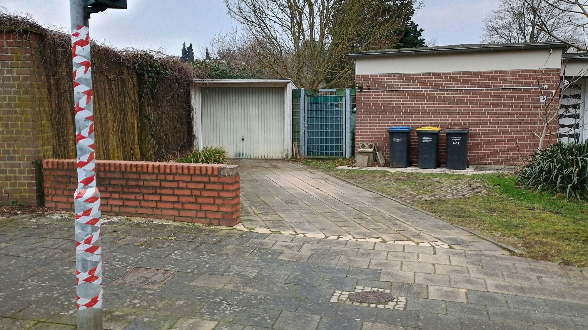 Auf dem Bild ist der Ampelmast zu sehen, dahinter eine kleine Mauer, und wiederum dahinter ein Garagentor.