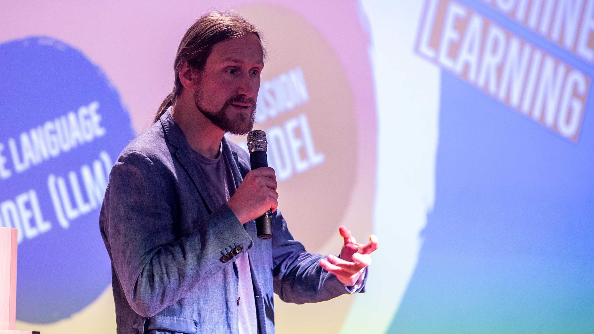 Frank Schlegel bei seinem Vortrag. Er hält ein Mikrofon in der Hand und gestikuliert.