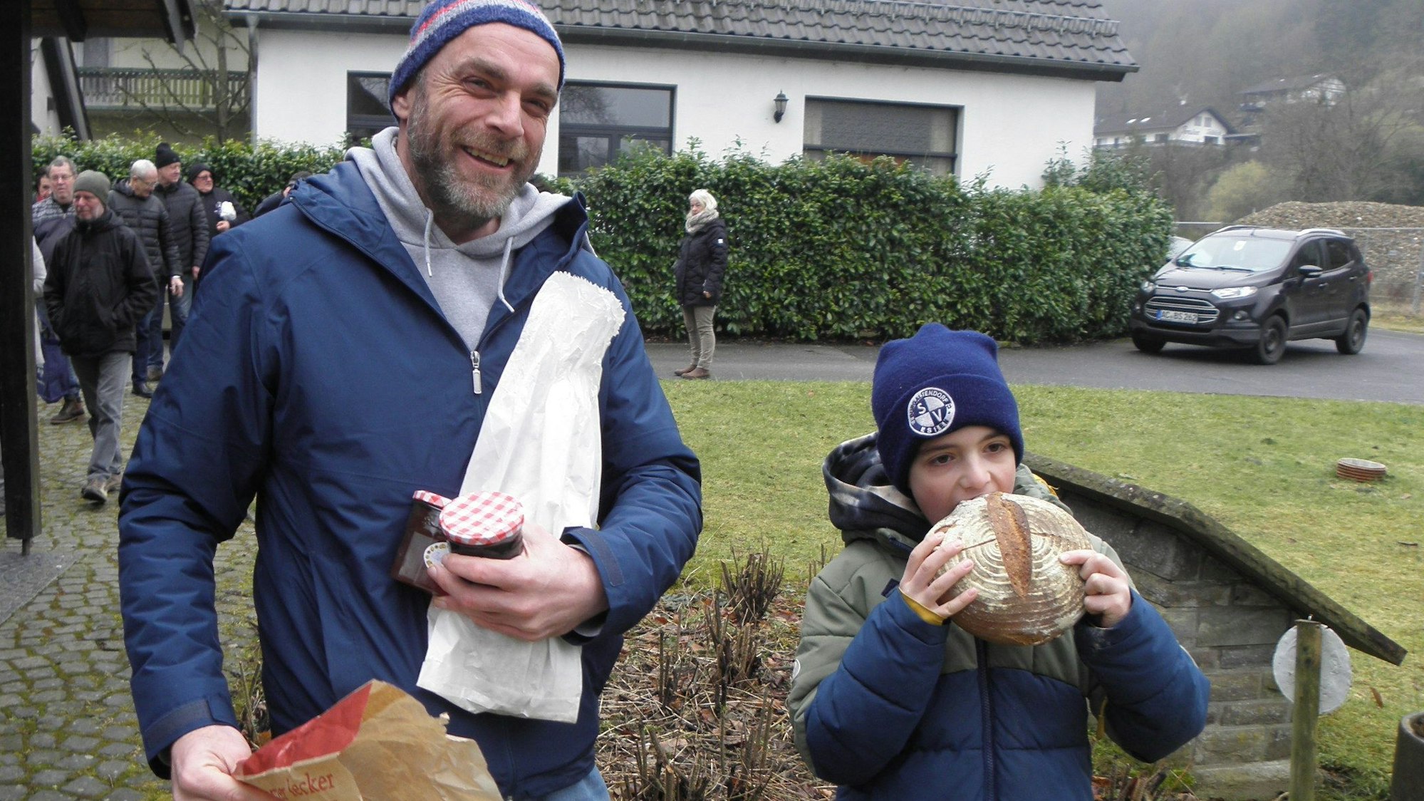 Ein Junge beißt in ein frisches Brot. Neben ihm steht sein Vater und lacht.