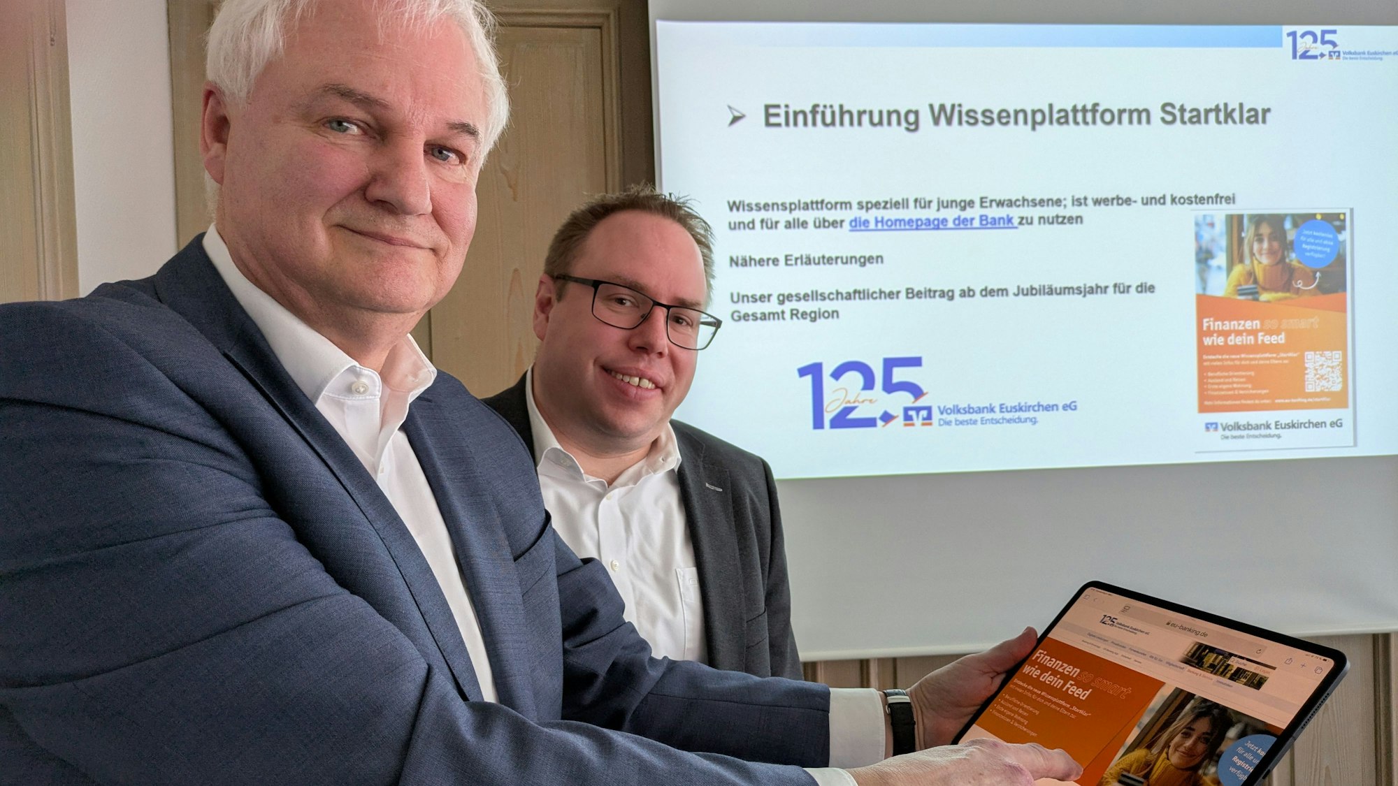 Hans-Jürgen Lembicz hält ein Tablett in der Hand, auf dem die „Startklar“-Seite zu sehen ist. Marc Güttes steht hinter ihm und schaut zu.