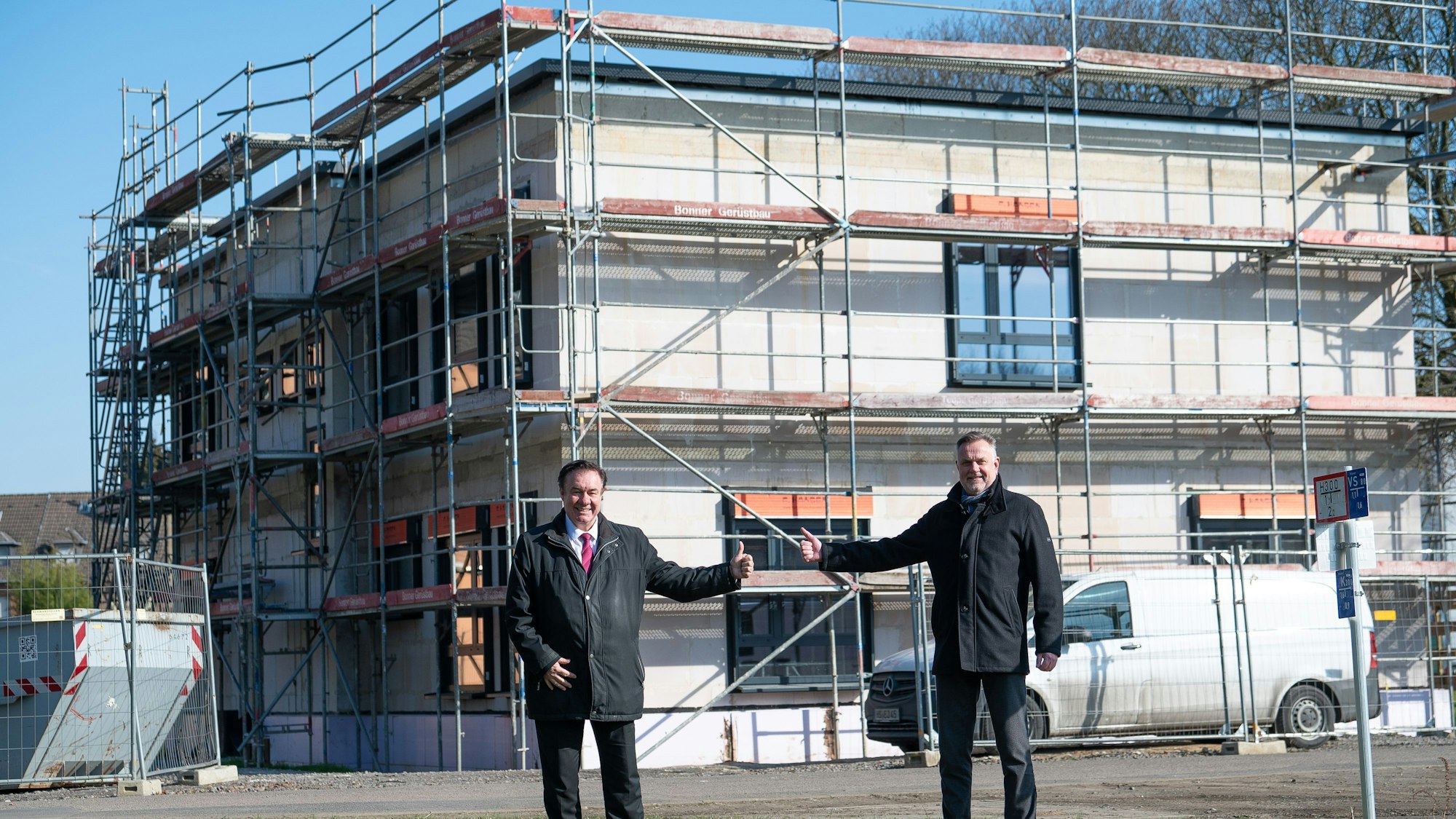 Das Foto zeigt zwei Männer vor dem eingerüsteten zweigeschossigen Rohbau.