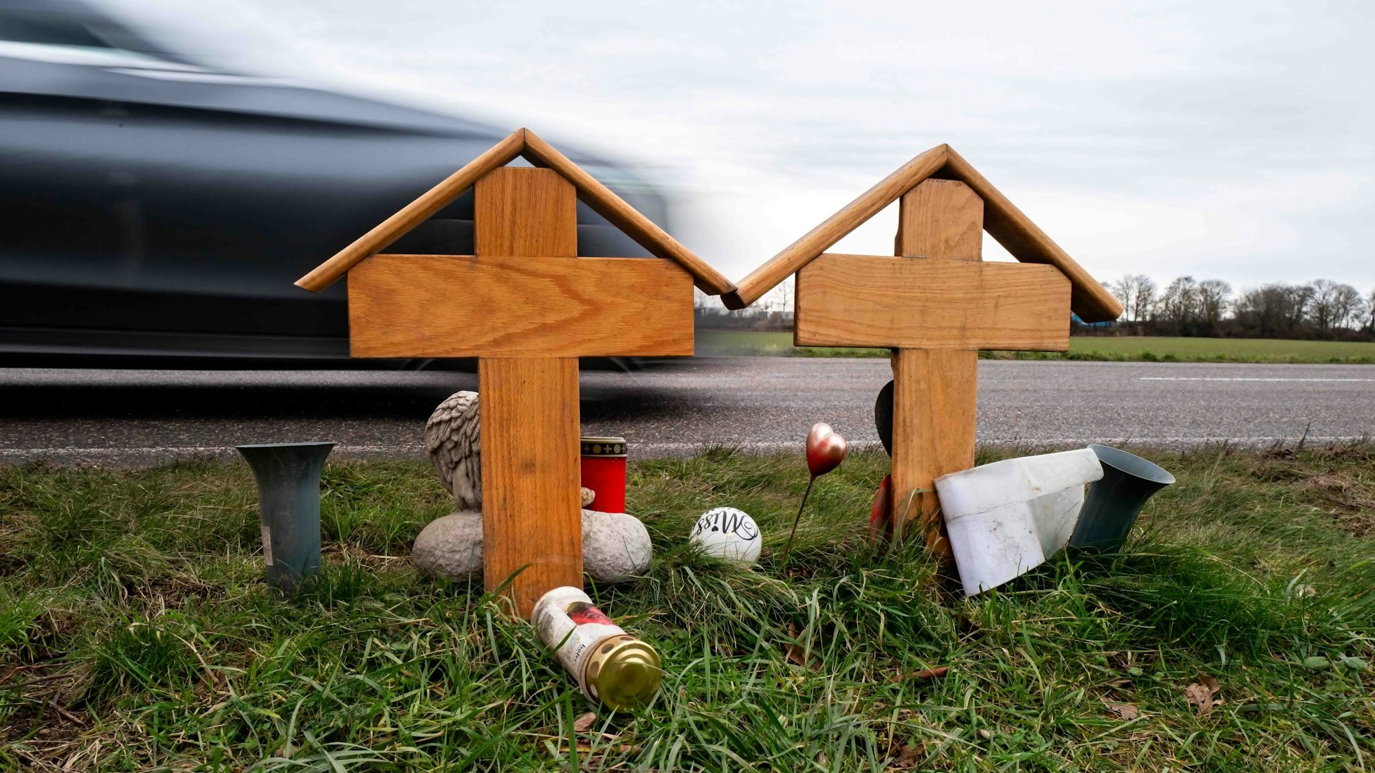 Am Straßenrand stehen zwei Holzkreuze, Grablichter und Blumenvasen.