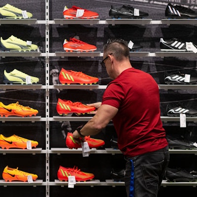 Ein Mitarbeiter Sportgeschäfts sortiert Fußballschuhe in einem Regal.