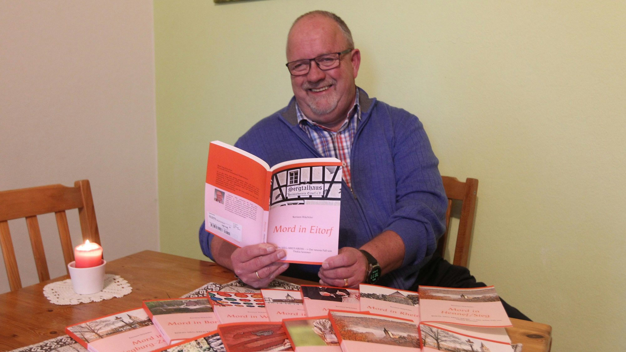 Ein Mann sitzt vor vielen Büchern an einem Tisch.