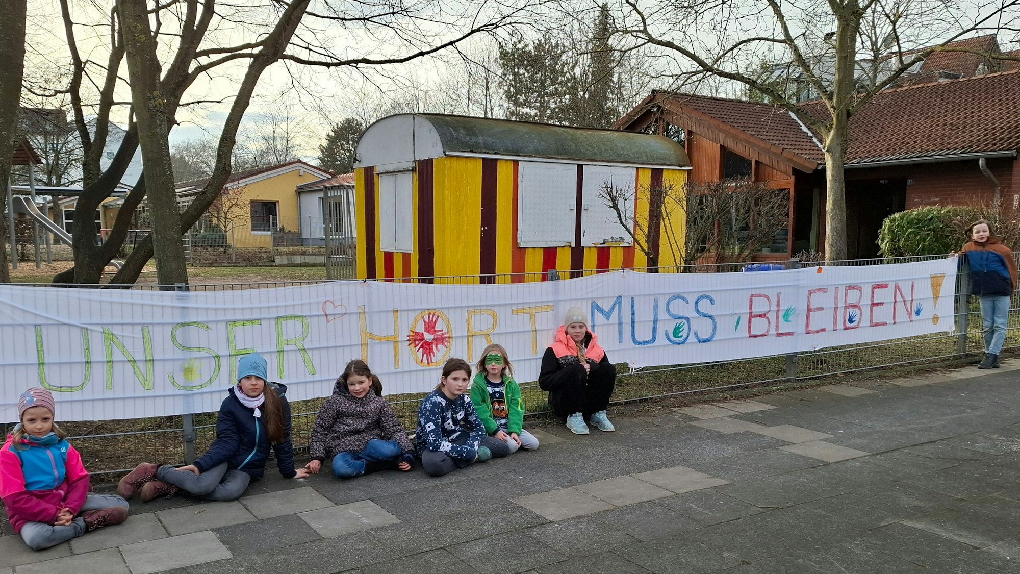 Auf dem Bild sind Kinder vor dem Hort vor einem selbst gemalten Transparent zu sehen.