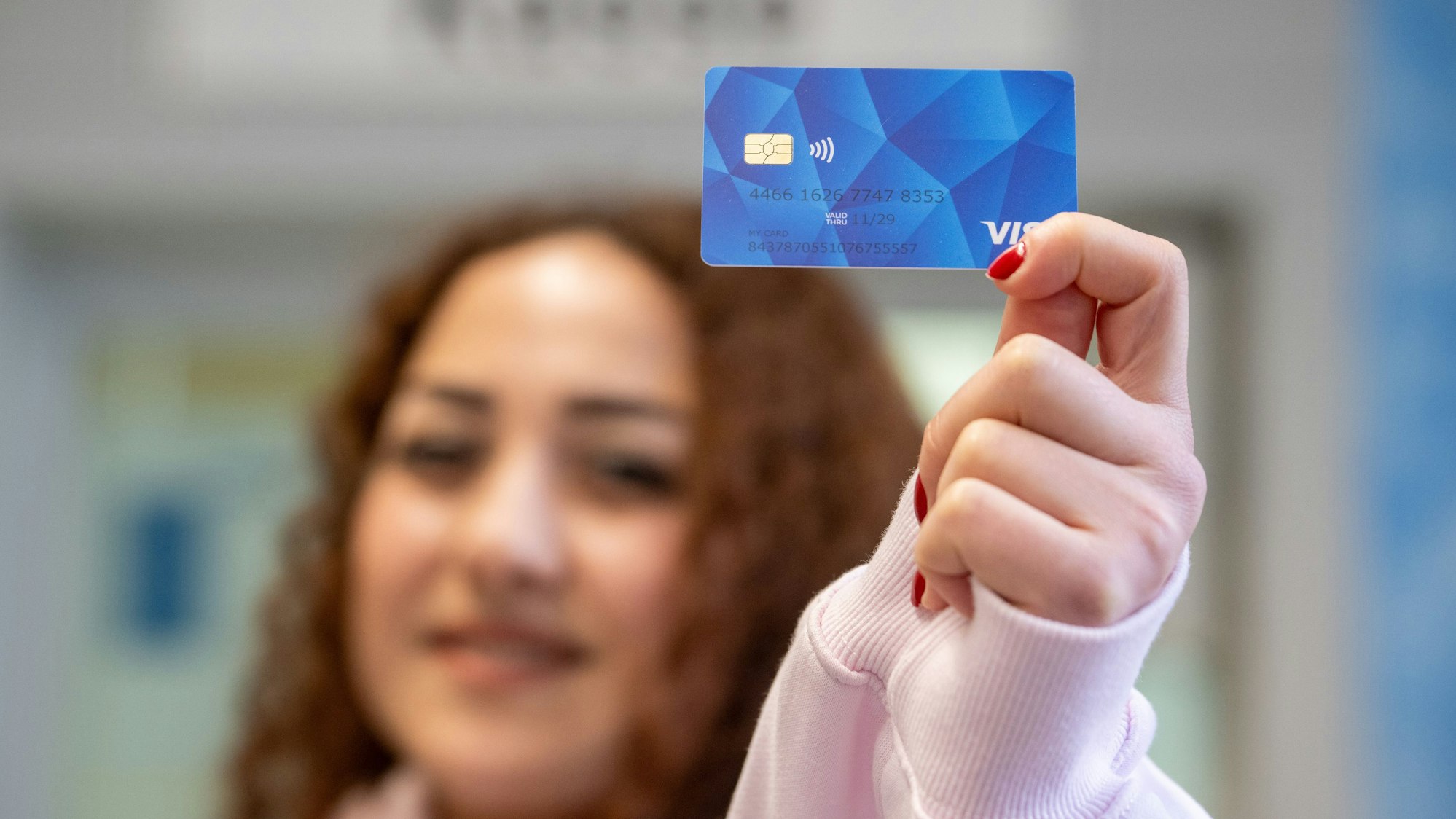 Eine Frau (verschwommen, im Hintergrund) hält eine Bezahlkarte in die Kamera. +++ dpa-Bildfunk +++