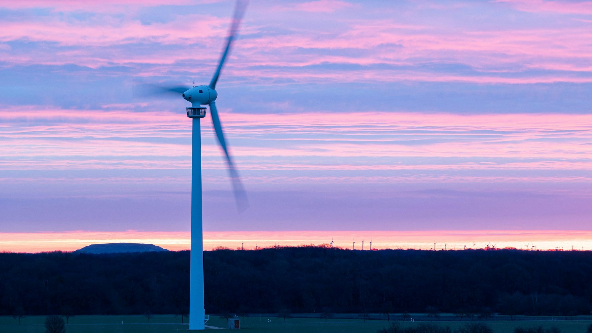 Die Rotorblätter einer Windkraftanlage drehen sich während der Morgendämmerung.
