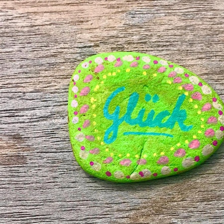Auf einem Stein, der angemalt wurde, steht „Glück“.