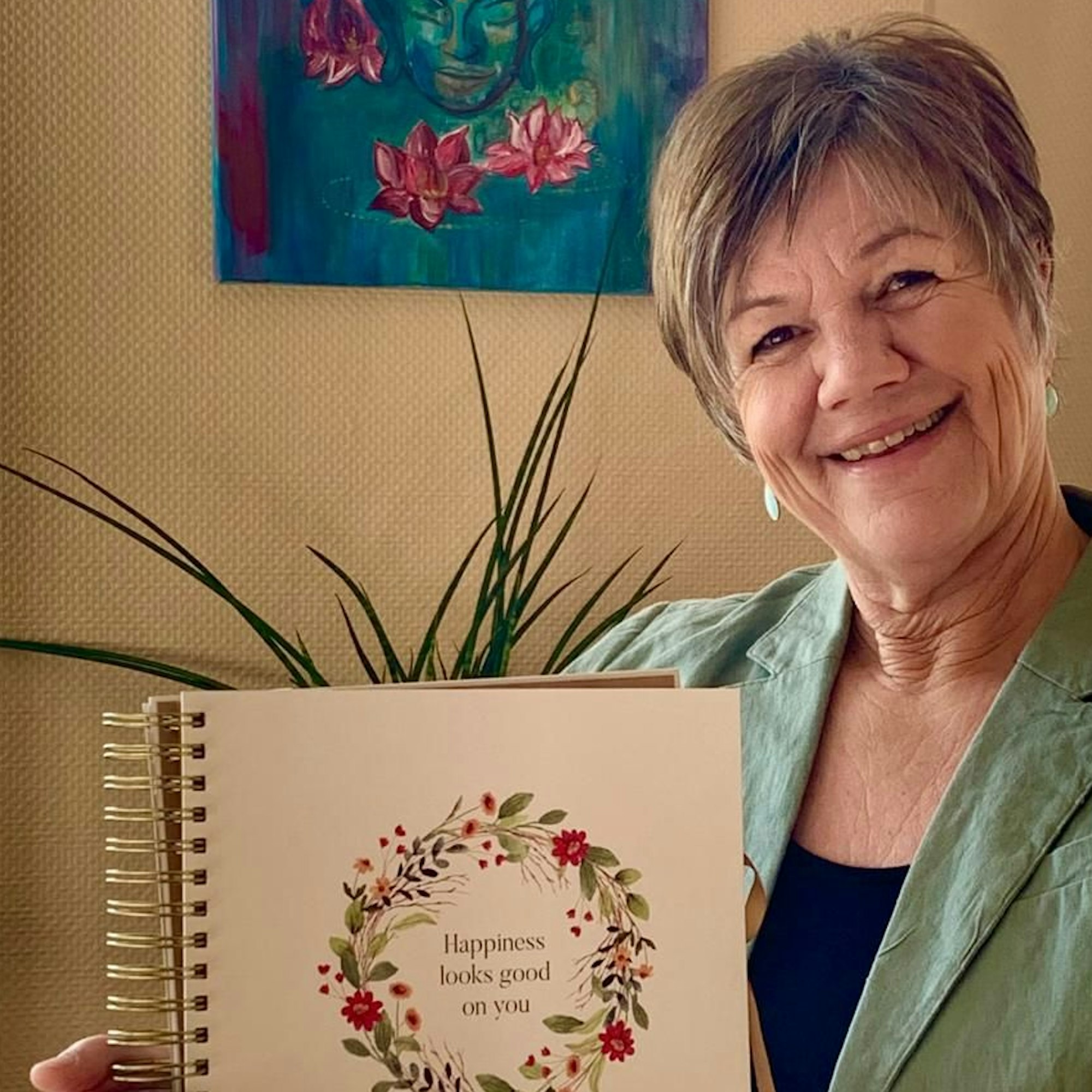 Eine Frau hält lächelnd ein Buch vor sich, auf dem „Happiness looks good on you“ steht.